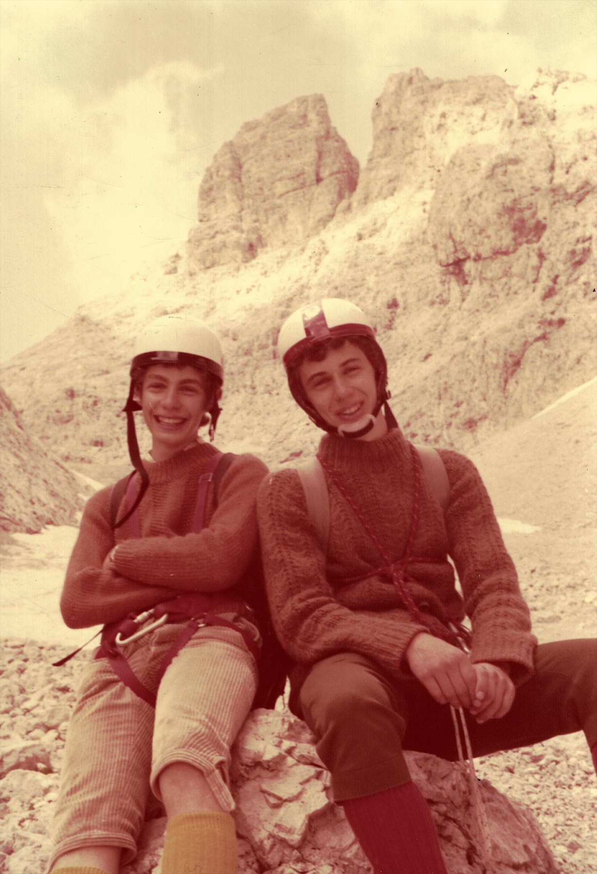 Due ragazzi con il casco seduti sulla roccia, con le Odle alle spalle, 1975